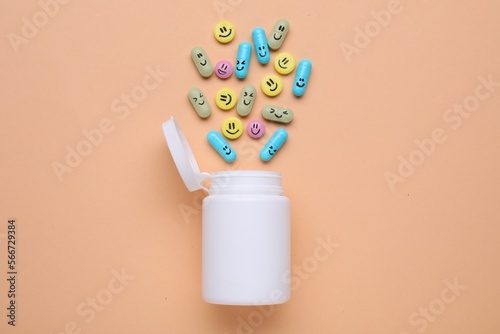 Bottle and antidepressant pills with funny faces on pale orange background, flat lay photo