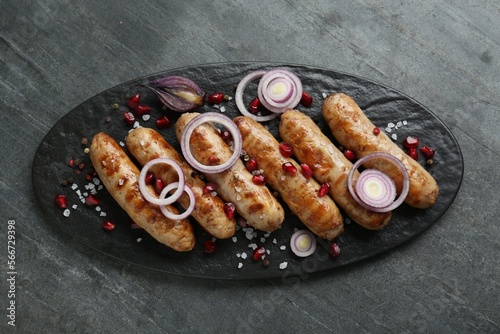 Tasty grilled sausages with onion rings and pomegranate seeds served on grey table, top view