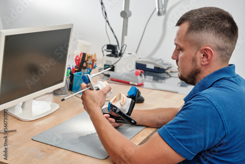 Dental technician working with articulator in dental laboratory.