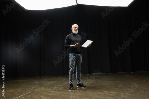 full length of mature tattooed actor pointing at screenplay on stage in theater.