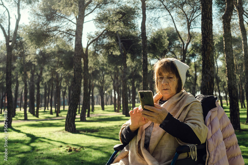 An elderly lady in a wheelchair in the park with her cell phone