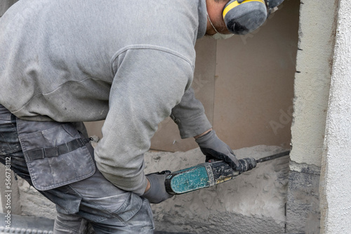 Builder worker with rotary hammer destroying beton wall.