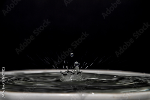 Clean water drops into clean water in white cup with black background