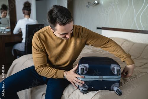 Man caucasian couple packing or unpack wardrobe cloth from suitcase at hotel room while his wife or girlfriend sit in background travel and vacation concept copy space © Miljan Živković