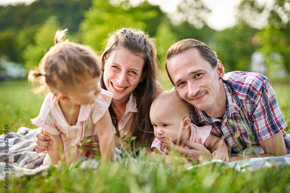 Happy family laying on a picnic blanket in nature - Parenthood and childhood family concept outdoors in a park Happy family laying on a picnic blanket in nature - Parenthood and childhood family concept outdoors in a park