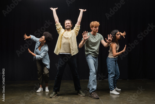 Quadro su tela young man standing with raised hands and closed eyes near multiethnic students rehearsing on stage in theater