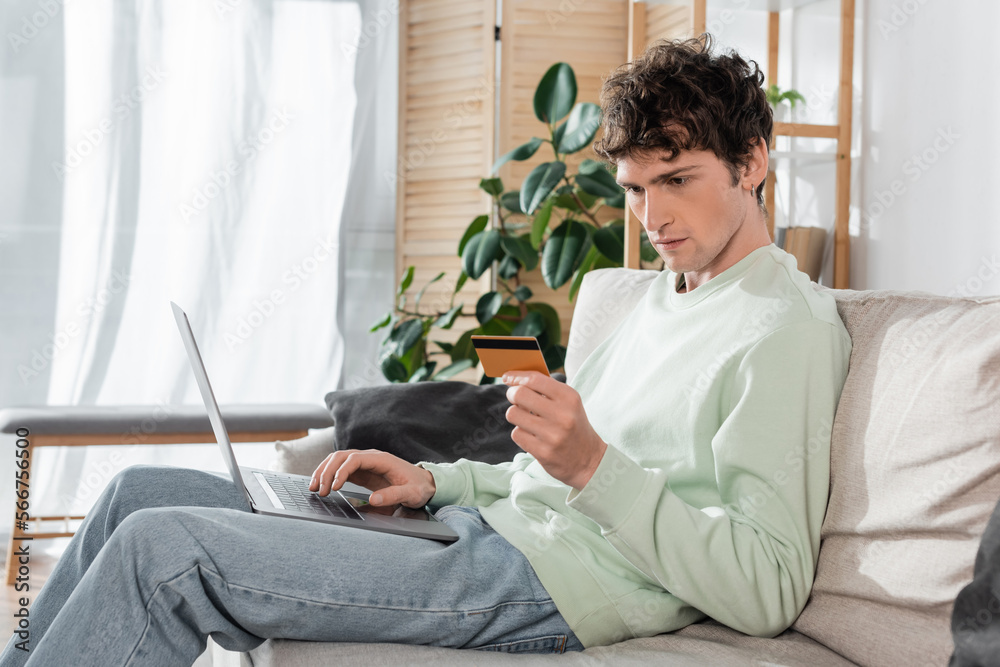 focused young man holding credit card while doing online shopping on laptop.