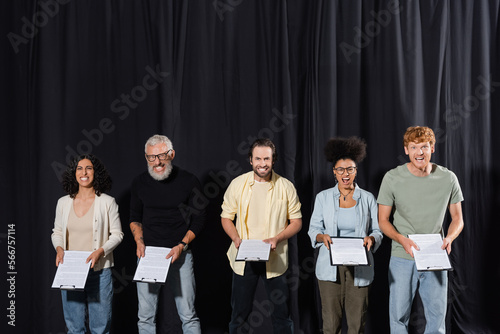 multicultural actors with bearded screenwriter holding clipboards and grimacing at camera during acting skills lesson. photo