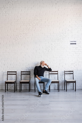 bored grey haired man sitting on chair near white wall and waiting for casting.