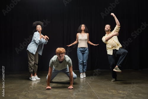 full length of multiethnic actors rehearsing in different poses on stage in theater.
