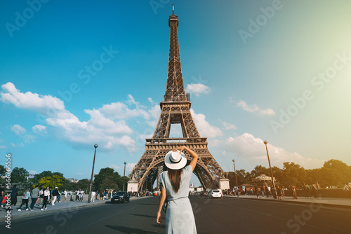 Rear view of woman tourist in sun hat standing in front of Eiffel Tower in Paris. Travel in France, tourism concept. Holiday or vacation in Paris © Creative Cat Studio