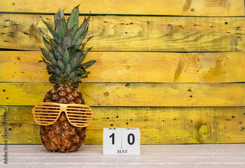 Creative May calendar planner with number  10. Pineapple character on bright yellow summer wooden background with calendar cubes. photo