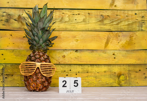 Creative july calendar planner with number  25. Pineapple character on bright yellow summer wooden background with calendar cubes. photo