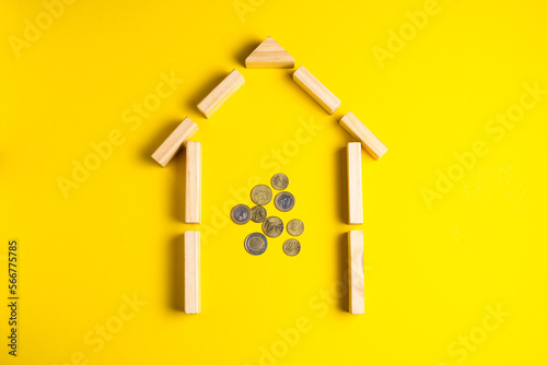 Wooden house model with coins, money, copy space on yellow background.