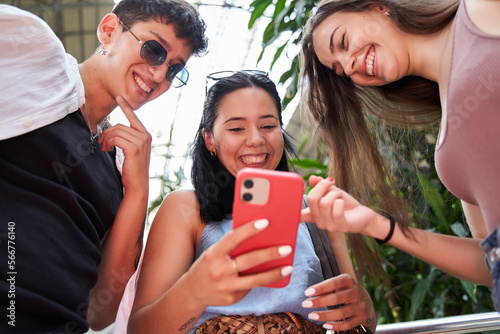 three friends looking at the cell phone from below. selective focus of a woman showing her smart phone while laughing.