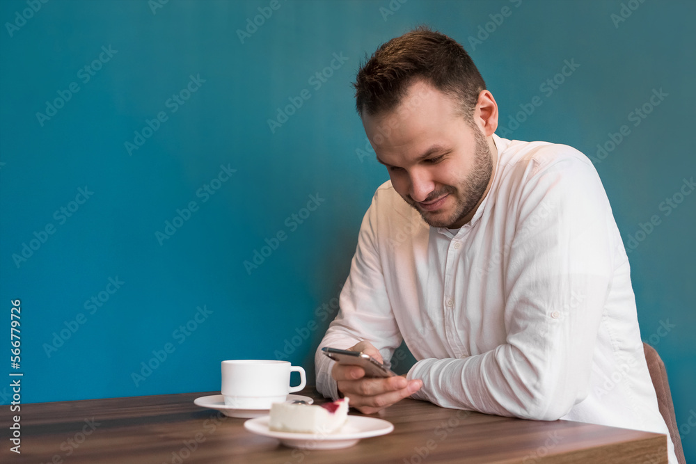 A young attractive European businessman spends time in a smartphone on coffee break sitting at a table in a cafe A young attractive European businessman spends time in a smartphone on coffee break sitting at a table in a cafe