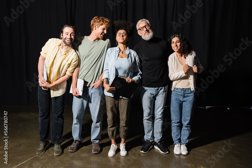 young emotional actors standing on theater stage near grey haired screenwriter.