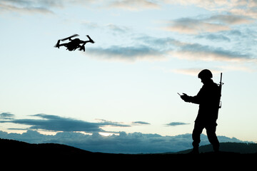 Silhouettes of soldiers are using drone and laptop computer for scouting during military operation against the backdrop of a sunset. Greeting card for Veterans Day, Memorial Day, Independence Day.