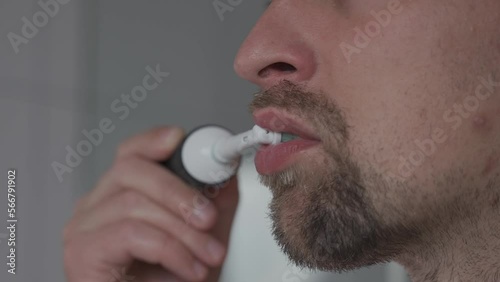 Man brushes his teeth with an electrical tootbrush at morning bathroom before work. Male uses an electric sonic dental cleaning brush. Daily dental hygiene and oral health with eletrical teethbrush.  photo