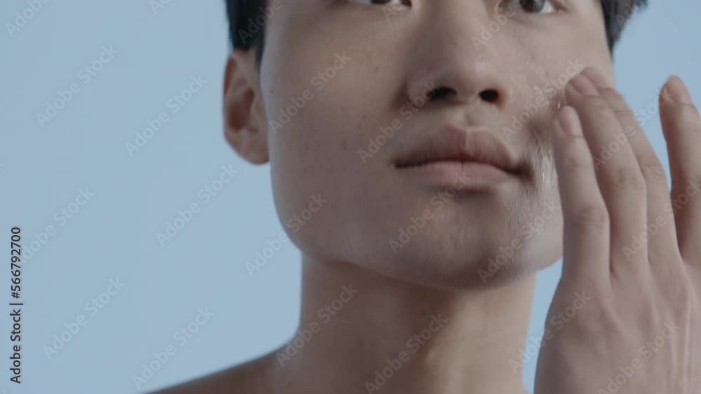 Portrait of handsome 20s Asian male using facial serum against blue background. Daily men skincare routine