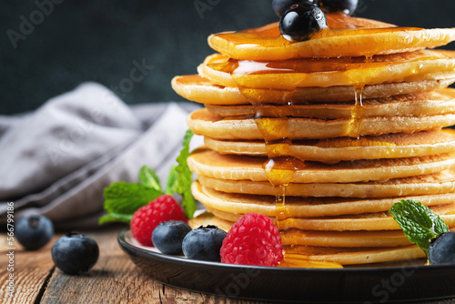 Delicious pancakes, with fresh blueberries, raspberry and maple syrup or honey on a dark background