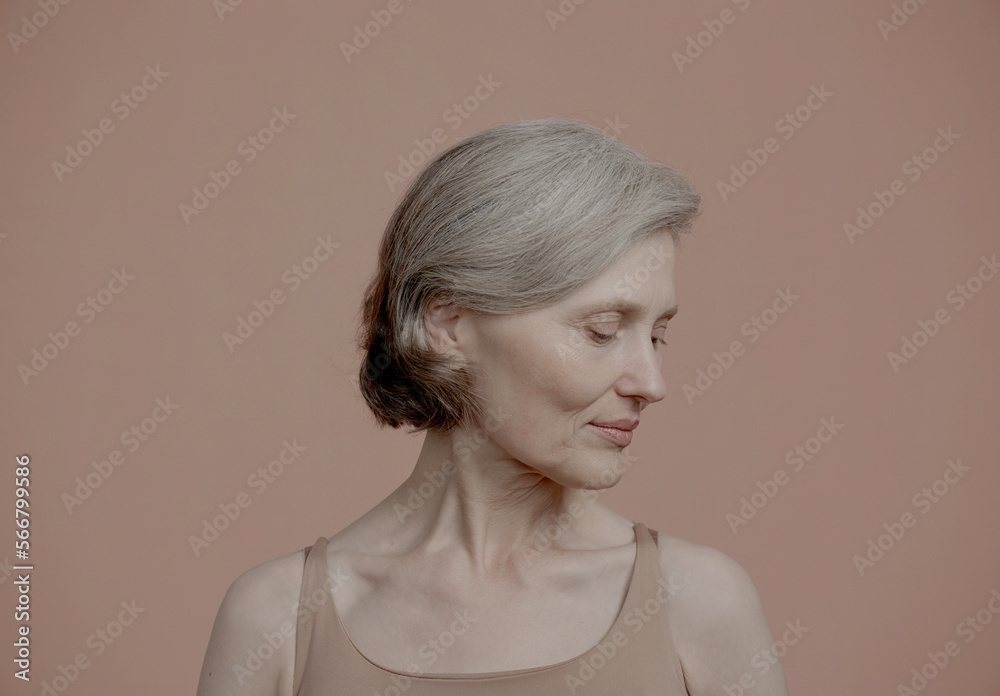 CU Portrait of beautiful 60s grey-haired mature senior adult female posing without makeup against light brown background. Studio shot, soft lighting. No make up, clean skin CU Portrait of beautiful 60s grey-haired mature senior adult female posing without makeup against light brown background. Studio shot, soft lighting. No make up, clean skin