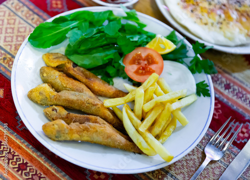 Appetizing roasted red mullet with side dish of fried potatoes  fresh greens and vegetables. Typical Turkish dish.