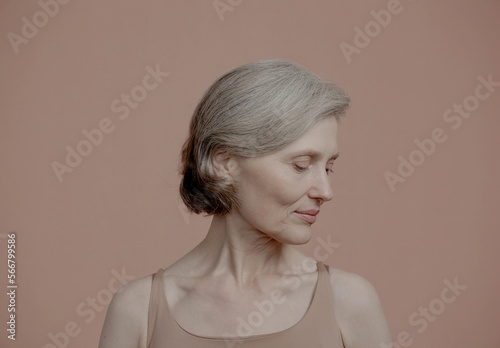 CU Portrait of beautiful 60s grey-haired mature senior adult female posing without makeup against light brown background. Studio shot, soft lighting. No make up, clean skin