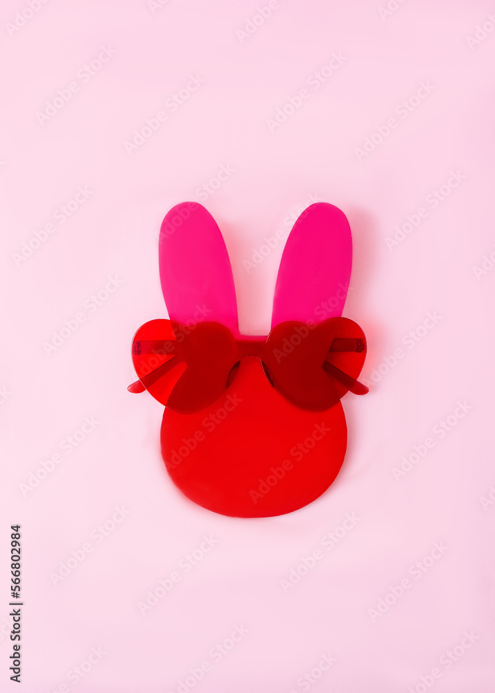A bunny red and fuchsia head with red sunglasses shaped as hearts against pink background. Minimal surreal concept for Easter card or banner. Flat lay.