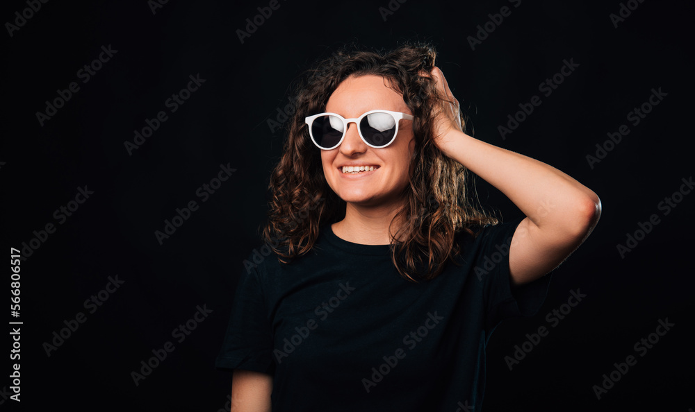 Portrait of a young curly woman wearing sunglasses and touching her head.