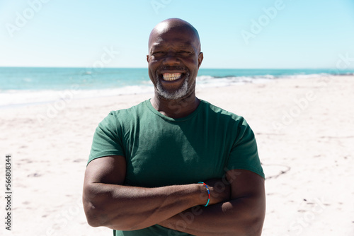 Portrait of african american senior man with arms crossed smiling and standing against sea and sky