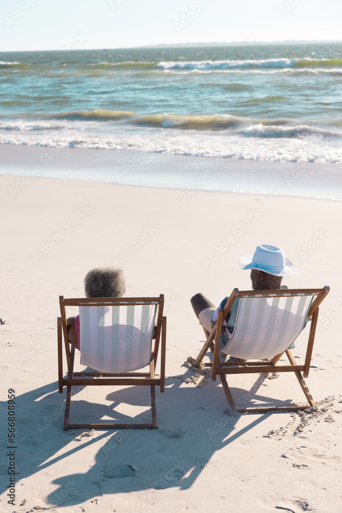Rear view of african american senior couple looking at seascape and relaxing on deckchairs at beach Rear view of african american senior couple looking at seascape and relaxing on deckchairs at beach