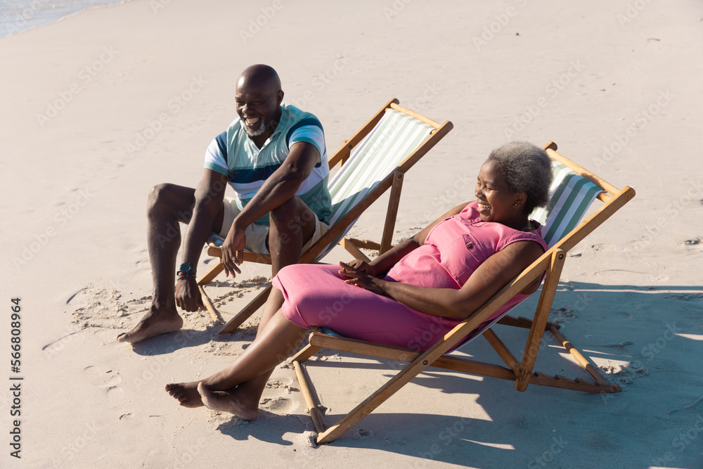 High angle view of happy african american senior couple sitting on deckchairs and talking at beach