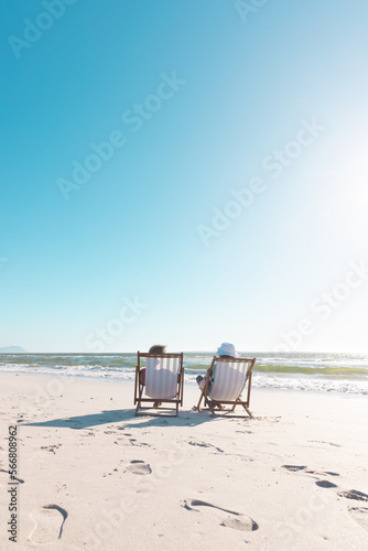 Canvas Print African american senior couple relaxing on deckchairs in front of sea under clea