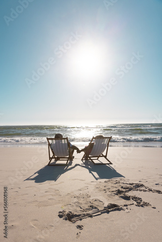 African american senior couple holding hands and relaxing on deckchairs in front of seascape