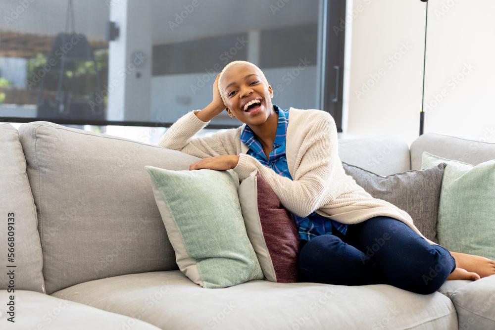 Fototapeta premium Portrait of happy african american woman sitting on sofa, looking at camera and smiling
