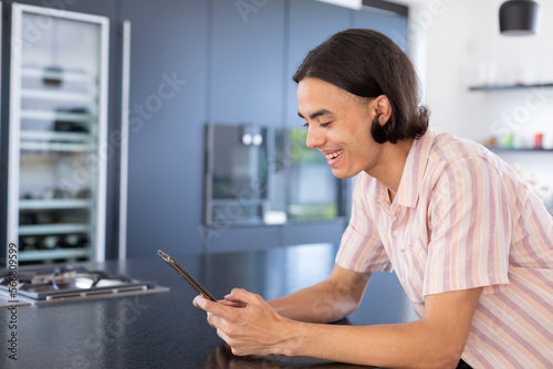 Happy biracial man using tablet in kitchen
