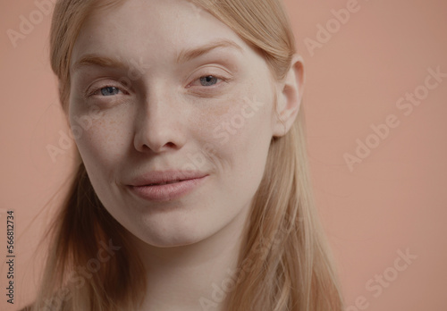 Beautiful young woman with absolutely no makeup gently smiles against neutral brown pastel background. Studio shot, soft lighting