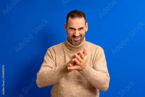 Close-up portrait of cunning, evil, cunning and scheming man, man trying to plot, plan something, screw up, hurt someone, isolated on blue background. Negative human emotions, facial expressions.