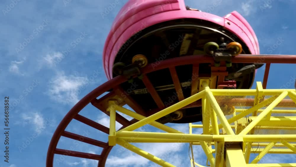 close up view of roller coaster trolley at amusement park against blue sky. pink trolley with unrecognizable people passes quickly along rails. Weekend with whole family on rides. close up view of roller coaster trolley at amusement park against blue sky. pink trolley with unrecognizable people passes quickly along rails. Weekend with whole family on rides.