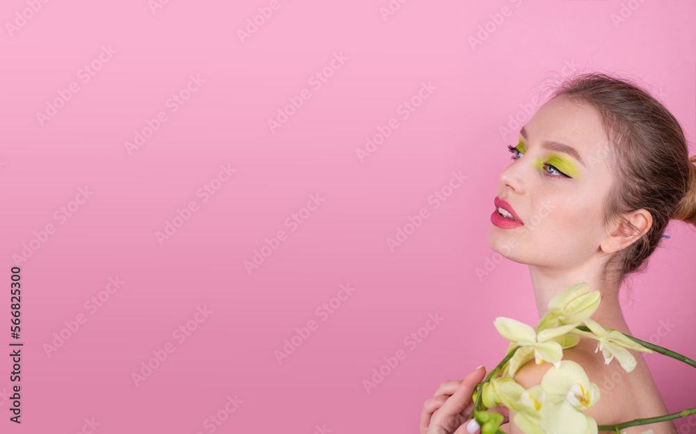 Fototapeta premium Young woman with spring make up holding flowers isolated on pink background Close up portrait Banner Space for text on the left