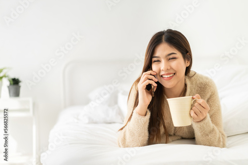 Portrait of smiling happy beauty pretty asian woman relaxing drinking cup of hot coffee or tea.Girl felling enjoy use smartphone having breakfast in holiday morning vacation on bed at home