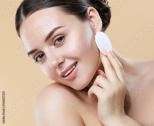Young woman removing makeup, holds cotton pads near face.