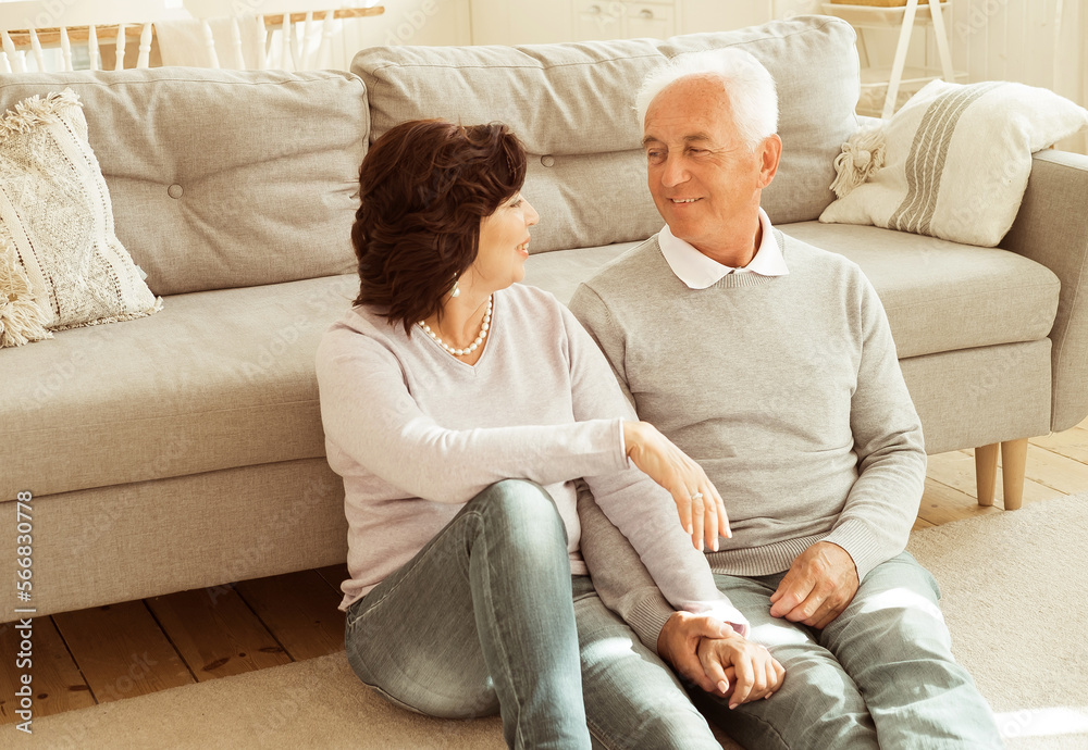 An elderly couple hugging while sitting on the floor of the living room. Relationship and family concept. An elderly couple hugging while sitting on the floor of the living room. Relationship and family concept.