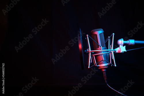a black microphone on black background under the neon light. podcasting, singing, and recording background.