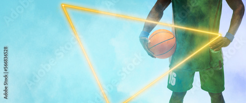 Midsection of african american player with basketball and hand on hip by triangle on blue background