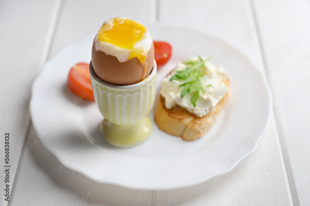 Fototapeta premium Fresh soft boiled egg in cup and sandwich on white wooden table