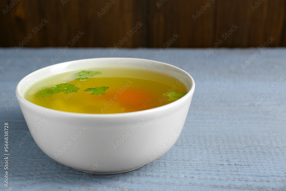 Delicious chicken bouillon with parsley on grey wooden table, closeup. Space for text