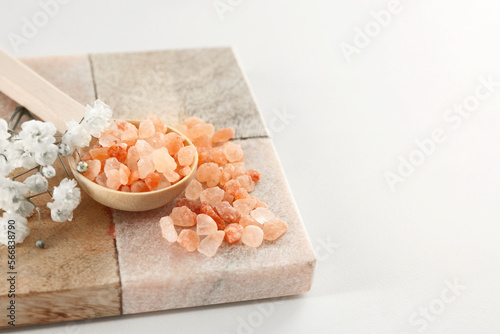 Orange sea salt and beautiful flowers on white table, closeup. Space for text