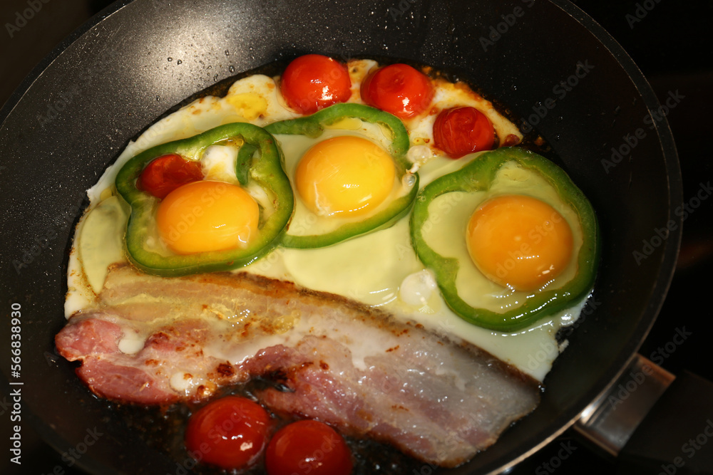 Cooking eggs with bacon, tomatoes and pepper in frying pan, closeup Cooking eggs with bacon, tomatoes and pepper in frying pan, closeup